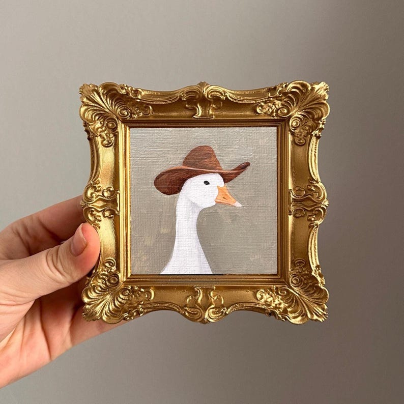 May include: A framed painting of a white goose wearing a brown cowboy hat. The painting is set in a gold ornate frame. The goose has an orange beak and is set against a neutral background.