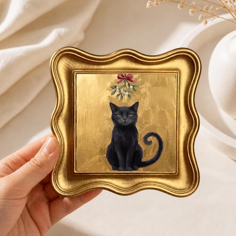 May include: A square wall art piece featuring a black cat sitting under a sprig of mistletoe with a red bow, set against a textured gold leaf background. The artwork is encased in a decorative, wavy-edged gold frame with a metallic finish.