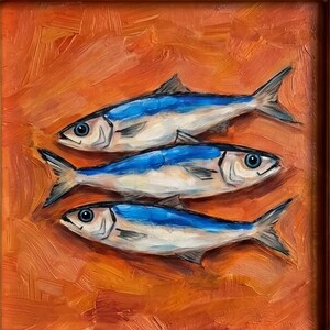 May include: Oil painting of three fish with blue and white bodies, set against an orange background. The fish are arranged horizontally, with visible details in their fins and eyes. The artwork is framed in a brown wooden frame.