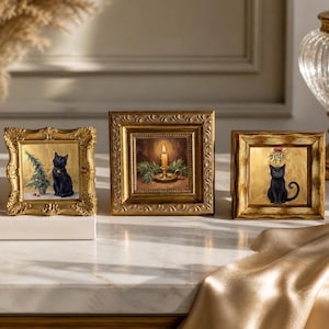 May include: Three square, ornate gold frames containing holiday-themed artwork. The left frame shows a black cat beside a small Christmas tree. The center frame depicts a lit candle in a holder with pine branches. The right frame features a black cat.
