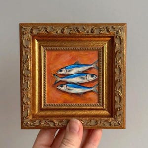 This small original artwork features vibrant blue fish against a warm orange background, bringing color and personality into everyday spaces. The ornate frame adds a refined, collected look that works beautifully in modern and classic interiors.