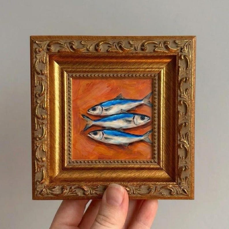 This small original artwork features vibrant blue fish against a warm orange background, bringing color and personality into everyday spaces. The ornate frame adds a refined, collected look that works beautifully in modern and classic interiors.