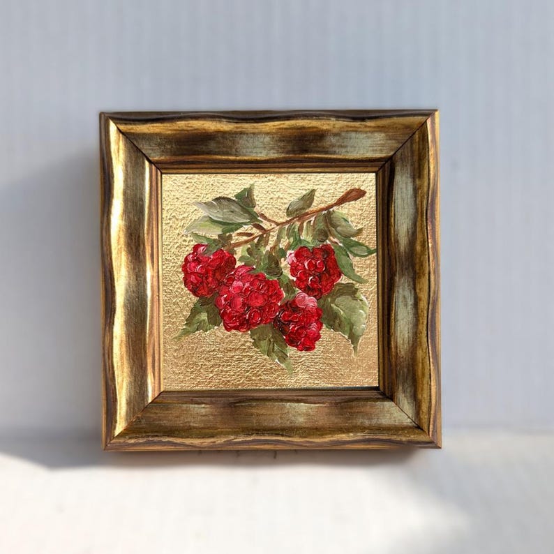 May include: A framed painting of a raspberry branch with vibrant red berries and green leaves. The artwork is set against a textured gold background and encased in a decorative, ornate gold-toned frame. The painting is a square format.