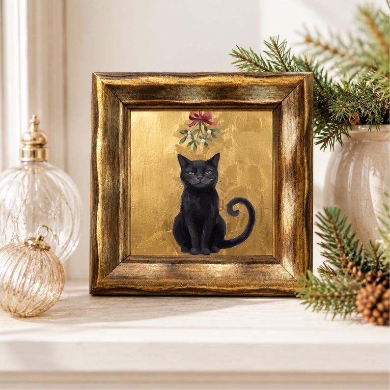 May include: A square framed wall art piece featuring a black cat sitting centered against a metallic gold background. Above the cat, a sprig of mistletoe with a red bow is depicted. The frame is dark, textured, and has a metallic gold finish.