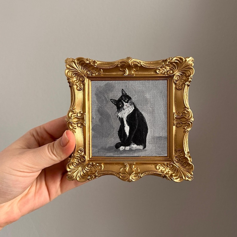 Miniature hand-painted tuxedo cat oil painting in a decorative gold frame held by a hand.