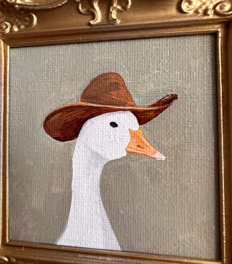 May include: A framed painting of a white goose wearing a brown cowboy hat. The goose has an orange beak and a black eye. The painting is set against a muted green background and framed in a gold-colored ornate frame.