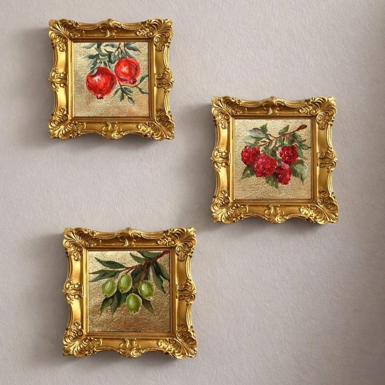 May include: Three small framed paintings with gold ornate frames. Each painting features a different fruit: pomegranates, raspberries, and olives. The paintings are on a gold background.