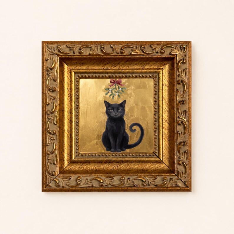 May include: A square framed painting featuring a black cat sitting centered against a textured gold leaf background. Above the cat, a sprig of mistletoe with a red bow is depicted. The artwork is encased in an ornate, antique gold-toned frame.