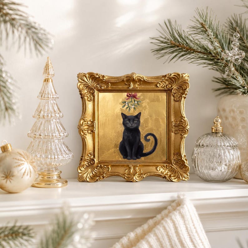 May include: A square framed artwork featuring a black cat sitting centered against a textured gold background. Above the cat, a sprig of green mistletoe is tied with a small red bow. The frame is ornate, metallic gold with intricate scrollwork details.