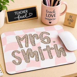 May include: A rectangular mouse pad featuring a light pink and white checkered pattern. The text "Mrs. Smith" is printed in the center in a bold, rounded font with a tan and black leopard print texture and a thin dark outline.