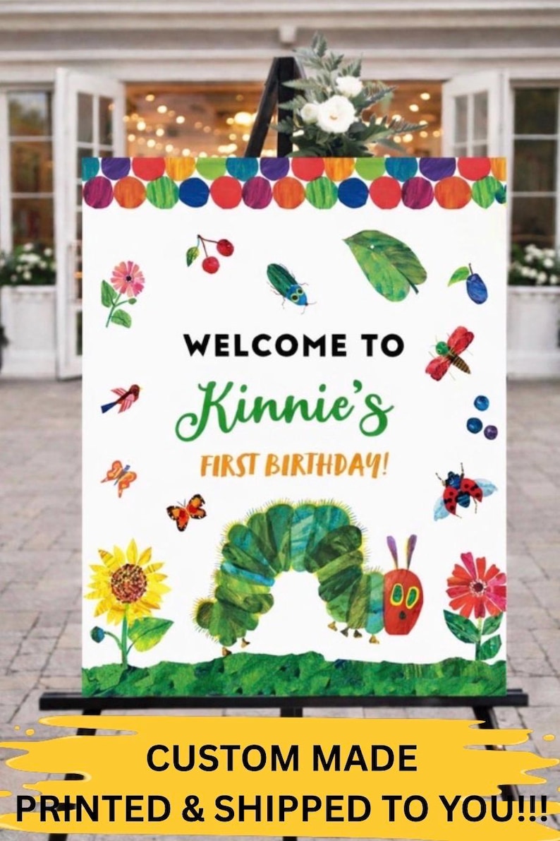 May include: A white sign with colorful polka dots, flowers, and insects, reads "WELCOME TO Kinnie's FIRST BIRTHDAY!". A large green caterpillar is featured at the bottom. The sign is displayed on a black easel.