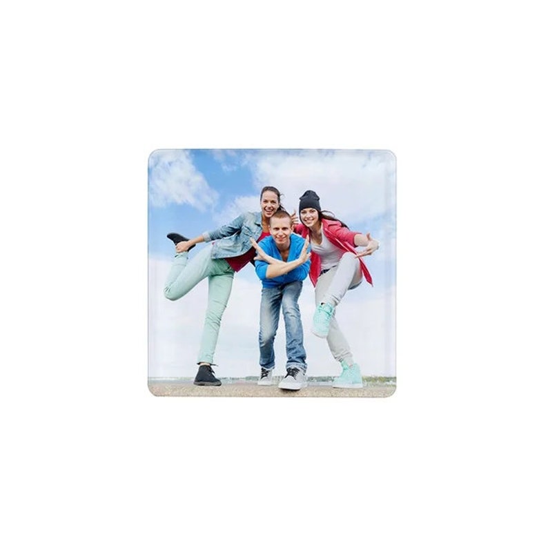 May include: Three friends pose for a photo, smiling and laughing. The woman on the left is wearing blue jeans, a blue denim jacket, and a white shirt. The woman on the right is wearing a red shirt, black pants, and a black beanie. The man in the middle is wearing a blue shirt, blue jeans, and a white shirt.
