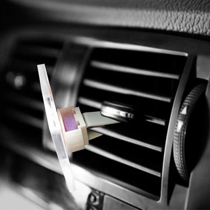 May include: A white car air freshener with a purple scent strip attached to a clear plastic clip. The clip is designed to fit into a car's air vent.