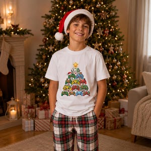 May include: A white short-sleeved t-shirt featuring a graphic of a Christmas tree constructed from colourful video game controllers, topped with a yellow star, paired with red, white, and green plaid pyjama trousers.