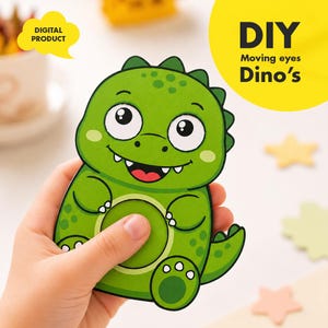 May include: A green dinosaur-shaped DIY craft with moving eyes, held by a hand. The dinosaur has a smiling face, white teeth, and a red mouth. The image includes the text "DIGITAL PRODUCT" and "DIY Moving eyes Dino's".