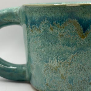 May include: A set of three ceramic mugs with a speckled, matte finish. Each mug features a different color: light blue, cream, and gray. The mugs have a simple, modern design, perfect for coffee or tea.