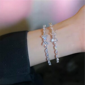 Puede incluir: Elegantes pendientes plateados con diseño floral. Cada pendiente presenta un grupo de cristales brillantes en la parte superior, con una delicada cadena de cristales más pequeños que caen en cascada. Los pendientes están diseñados para colgar y captar la luz.