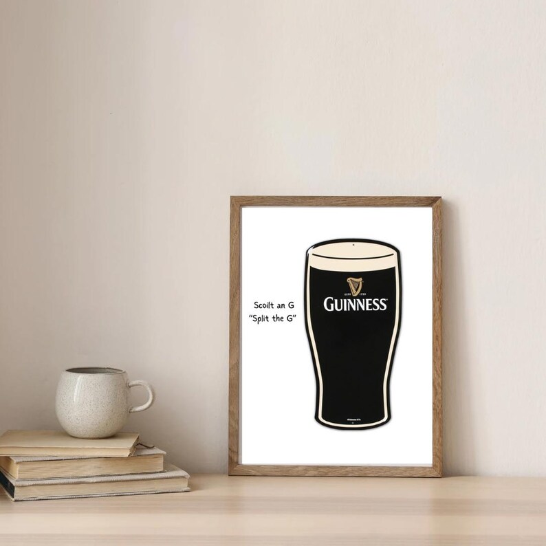 May include: A framed print featuring a stylized pint of Guinness stout. The black and white image includes the Guinness logo and the phrase "Scoilt an G, Split the G." The print is in a wooden frame, and the image is on a white background.