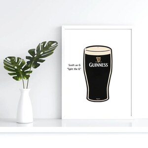 May include: A framed print featuring a pint of Guinness stout. The black and white image has the Guinness logo and text that reads "Scoilt an G Split the G". A white vase with green leaves is on the left.