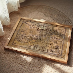 May include: A framed map with a vintage aesthetic, featuring detailed illustrations of a fantasy world. The map is in a wooden frame, resting on a beige carpet. The map's color palette includes beige, brown, and sepia tones, with intricate drawings of castles, creatures, and landmarks.