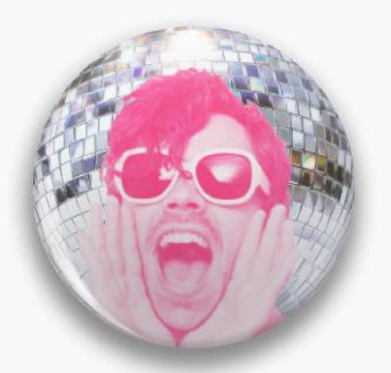 May include: A circular pin-back button featuring a monochromatic hot pink graphic of a person with their hands on their cheeks and mouth open in an expression of surprise, wearing white-rimmed sunglasses against a reflective silver disco ball.