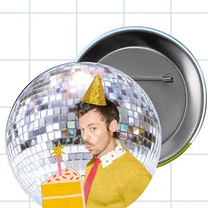 May include: A circular pin-back button featuring a disco ball background and a person wearing a gold glitter party hat, a yellow textured shirt with a white collar, and a red tie, holding a slice of yellow cake with a pink star-topped candle.