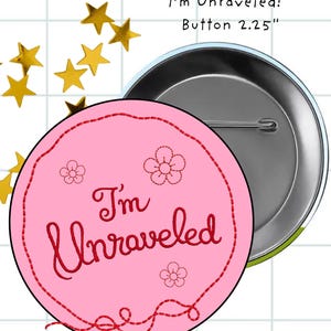 May include: A round pink button with a 2.25 inch diameter, featuring the text "I'm Unraveled" in red script, surrounded by a red stitched border and three small red flower outlines. The back of the button shows a silver metal pin mechanism.