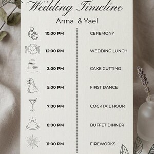 Könnte beinhalten: Eine Hochzeitszeitplan-Karte mit dem Text "Wedding Timeline Anna & Yael". Der Zeitplan umfasst Zeremonie, Hochzeitsessen, Anschneiden der Torte, Eröffnungstanz, Cocktailstunde, Buffet und Feuerwerk. Ein goldener Ehering befindet sich im Vordergrund.