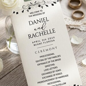 Peut inclure: Un programme de mariage crème avec les noms "Daniel et Rachelle" et les détails de la cérémonie. Le programme présente du texte noir et des motifs floraux. Des fleurs blanches et des alliances dorées sont en arrière-plan.