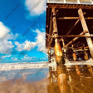 May include: A scenic photograph of a wooden pier extending into the ocean. The pier's weathered wood contrasts with the bright blue sky and fluffy white clouds. The water reflects the pier and sky.