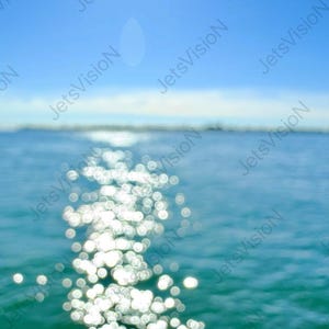 Può includere: Immagine sfocata di un corpo idrico sotto un cielo blu brillante. La luce del sole si riflette sull'acqua, creando un effetto scintillante. La linea dell'orizzonte è visibile in lontananza.