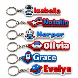 May include: Six custom keychains featuring space-themed icons and names. The designs include an astronaut with Isabella, a shooting star with Natalia, a robot with Harper, a UFO with Olivia, a rocket with Grace, and a planet with Evelyn in red, blue, and white.