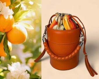 Elegant Orange Leather Bucket Bag with Braided Handle, Drawsting Clouser & Crossbody Strap. Women's barrel bag with decorative lining.
