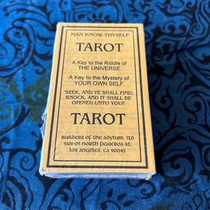 May include: A rectangular tarot deck box with a tan label and black text. The text reads: MAN KNOW THYSELF, TAROT, A Key to the Riddle of THE UNIVERSE, A Key to the Mystery of YOUR OWN SELF, SEEK, AND YE SHALL FIND; KNOCK, AND IT SHALL BE OPENED UNTO YOU!, TAROT, BUILDERS OF THE ADYTUM, LTD, 5101-05 NORTH FIGUEROA ST. LOS ANGELES, CA 90042.