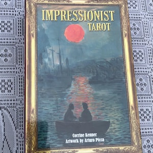 May include: The Impressionist Tarot deck has a gold-framed cover with the title "IMPRESSIONIST TAROT". The artwork depicts a boat with two figures, set against a dark blue background with a red sun. The artist's name is also included.