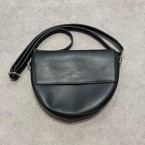 May include: Black crossbody bag with a curved bottom and a flap closure. The bag has a long, adjustable strap and the brand name "VALENTINO" is embossed on the front. The bag is made of a smooth, matte material.