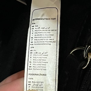 May include: A close-up of a tag with text in multiple languages, including English, French, and Spanish. The tag lists the materials used in a product, such as PVC, polyurethane, and polyester. The tag is white with black text.