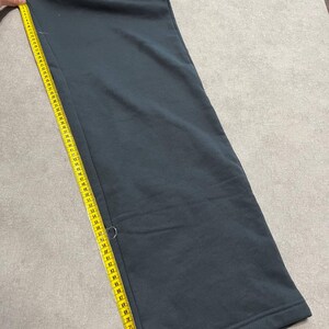 May include: Dark charcoal gray sweatpants featuring the white text 'alo' near the waistband. A yellow measuring tape is placed along the side seam, showing a length measurement extending past 30 inches on the tape's imperial scale.