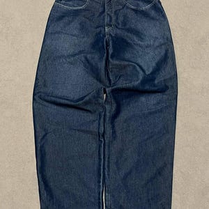 Puede incluir: Vaqueros de mezclilla azul oscuro con un corte relajado. Los vaqueros tienen un dise&ntilde;o cl&aacute;sico de cinco bolsillos, cierre de bot&oacute;n y cremallera, y la marca "TJ560" es visible en la cintura y una peque&ntilde;a etiqueta. Los vaqueros est&aacute;n planos sobre una superficie neutra.