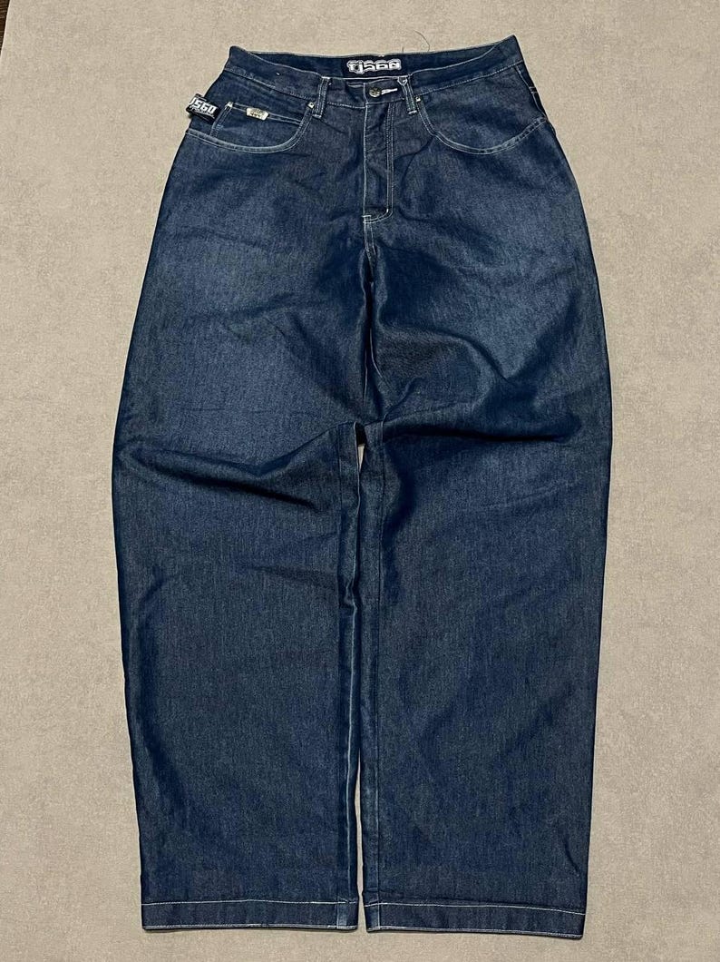 Puede incluir: Vaqueros de mezclilla azul oscuro con un corte relajado. Los vaqueros tienen un dise&ntilde;o cl&aacute;sico de cinco bolsillos, cierre de bot&oacute;n y cremallera, y la marca "TJ560" es visible en la cintura y una peque&ntilde;a etiqueta. Los vaqueros est&aacute;n planos sobre una superficie neutra.