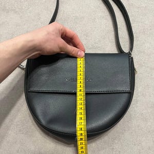 May include: Black crossbody bag with a flap closure. The bag is approximately 10 inches in length. The word "VALENTINO" is embossed on the flap. The bag has a long, adjustable strap.
