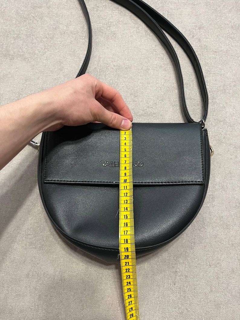 May include: Black crossbody bag with a flap closure. The bag is approximately 10 inches in length. The word "VALENTINO" is embossed on the flap. The bag has a long, adjustable strap.