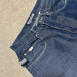 Puede incluir: Vaqueros de mezclilla azul oscuro con costuras blancas. Los vaqueros presentan la marca "TJ560" en una etiqueta y un bot&oacute;n met&aacute;lico. Los vaqueros tienen un dise&ntilde;o cl&aacute;sico de cinco bolsillos.