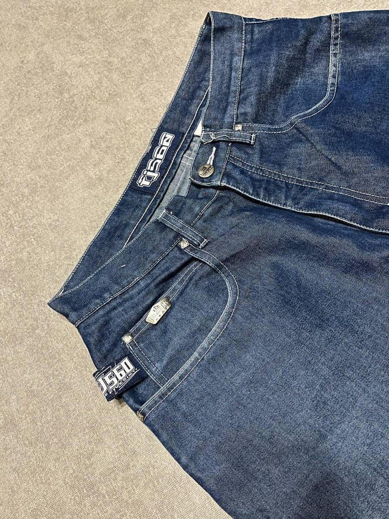 Puede incluir: Vaqueros de mezclilla azul oscuro con costuras blancas. Los vaqueros presentan la marca "TJ560" en una etiqueta y un bot&oacute;n met&aacute;lico. Los vaqueros tienen un dise&ntilde;o cl&aacute;sico de cinco bolsillos.