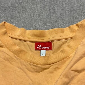May include: A light orange t-shirt with a crew neck. The red tag at the neck reads "Kreem" in white lettering. The shirt is a size large.