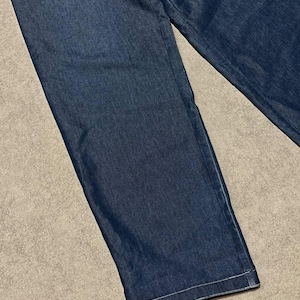 Puede incluir: Primer plano de unos vaqueros de mezclilla azul medio. Los vaqueros tienen un corte de pierna recta y est&aacute;n hechos de una tela de mezclilla resistente. El dobladillo est&aacute; acabado con una costura blanca.