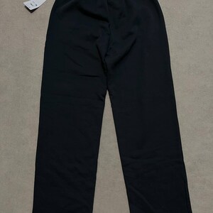 May include: Solid black trousers featuring a high-rise elasticated waistband with a gathered texture. The pants have a straight-leg cut and a clean, unadorned finish. A white rectangular retail tag is attached to the waistband by a black string.