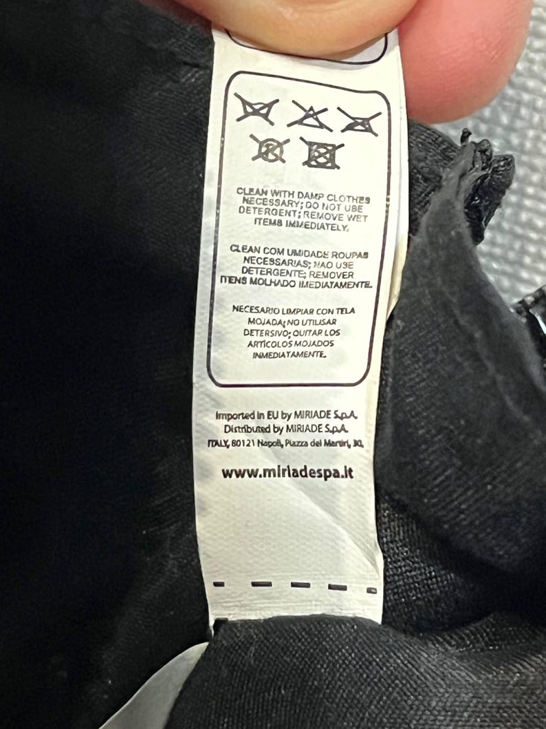 May include: A white clothing tag with care instructions and the text "CLEAN WITH DAMP CLOTHES NECESSARY; DO NOT USE DETERGENT; REMOVE WET ITEMS IMMEDIATELY." The tag also includes the website address www.miriadespa.it.
