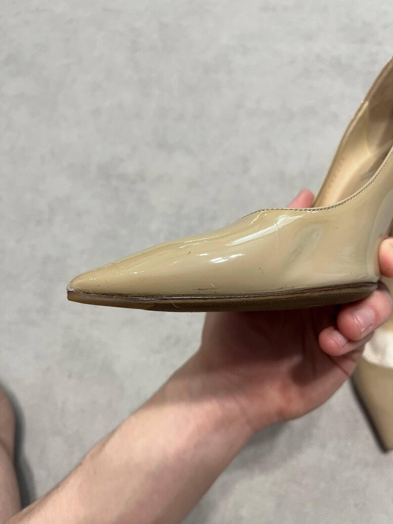 Puede incluir: Un par de zapatos de tac&oacute;n alto de charol beige con punta. Los zapatos tienen un acabado brillante y una suela marr&oacute;n. El tac&oacute;n no es visible en la imagen.