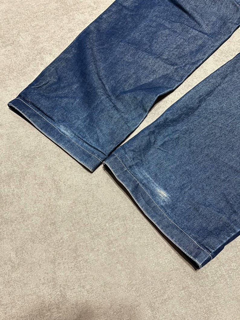 Puede incluir: Primer plano de dos perneras de pantal&oacute;n vaquero azul denim. Los vaqueros son de un lavado medio con costuras visibles a lo largo de los dobladillos. La tela muestra algo de desgaste, con algunas manchas m&aacute;s claras en el denim.